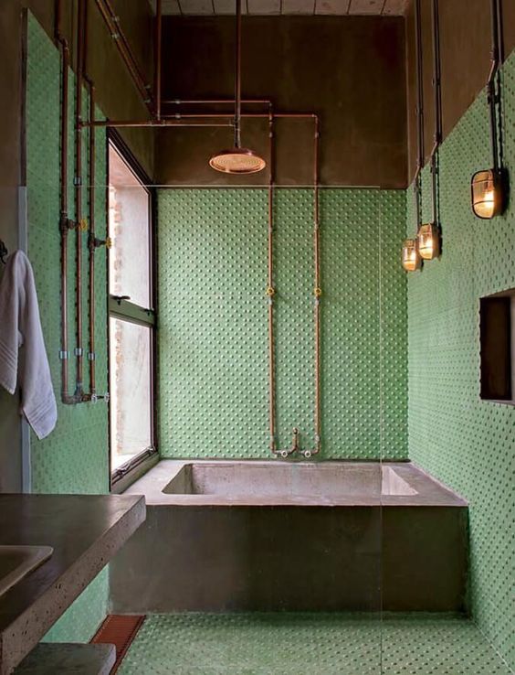 An-industrial-vintage-bathroom-with-polka-dot-tiles-a-concrete-tub-and-vanity-exposed-pipes-in-copper