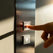 A woman's finger presses the elevator button in the sunlight
