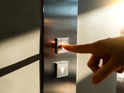 A woman's finger presses the elevator button in the sunlight