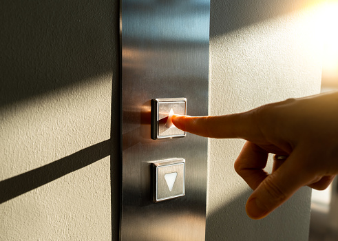 A woman's finger presses the elevator button in the sunlight