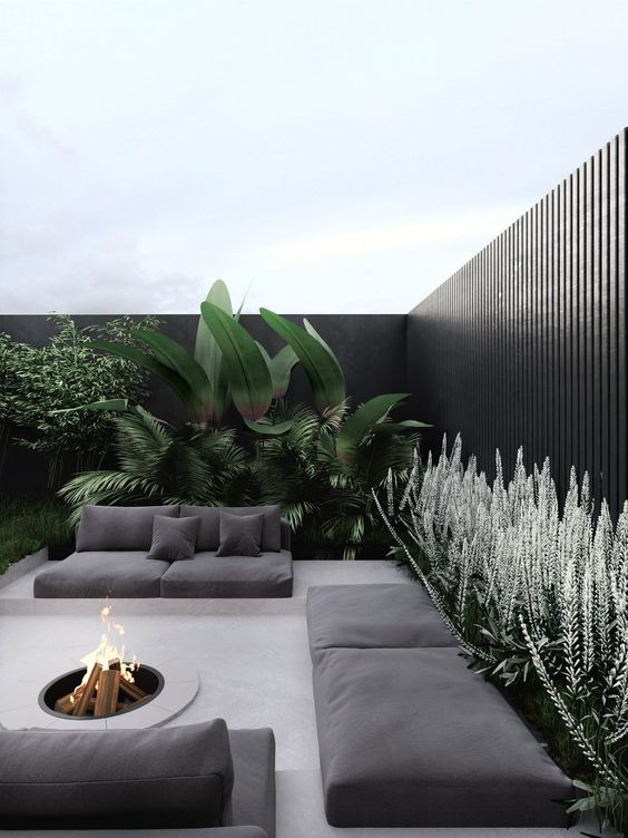 A-modern-tropical-backyard-with-grey-sofas-on-platforms-a-fire-pit-and-lots-of-lush-greenery-and-blooms