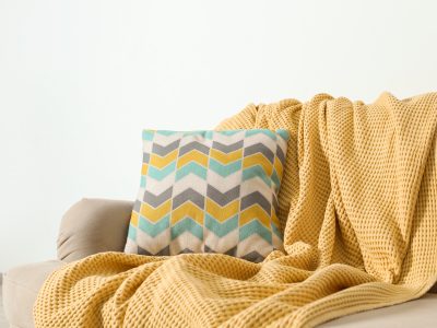 Cozy sofa with pillow and plaid near light wall. idea for living