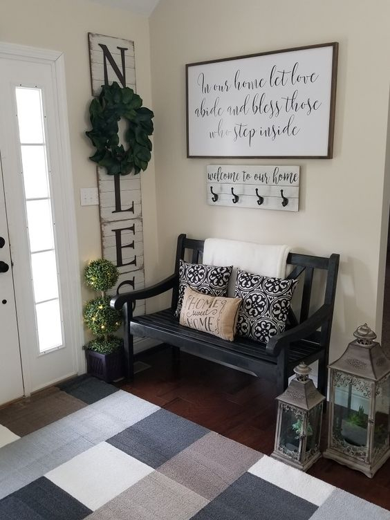 A-cozy-famrhouse-entryway-with-a-blakc-vintage-bench-candle-lanterns-a-sign-and-a-colored-rug