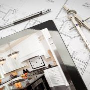 Computer tablet showing kitchen illustration on house plans, pencil, compass.