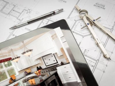 Computer tablet showing kitchen illustration on house plans, pencil, compass.
