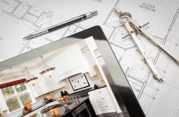 Computer tablet showing kitchen illustration on house plans, pencil, compass.
