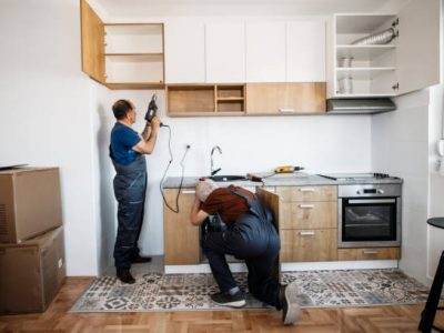 Two senior men, manual workers assembling kitchen furniture in new apartment