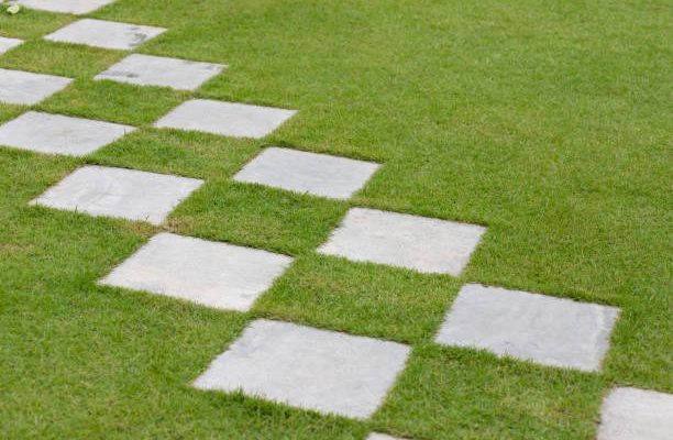 Square stone steps in the garden. concrete walk way path in green turf.