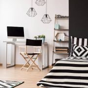 Black and white home interior with bed, pendant lamp, chair, desk and computer