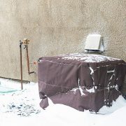 Residential air conditioning unit wrapped with protective cover in blizzard