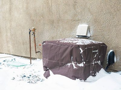 Residential air conditioning unit wrapped with protective cover in blizzard