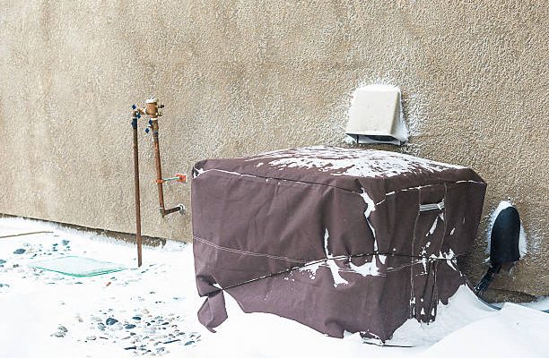 Residential air conditioning unit wrapped with protective cover in blizzard