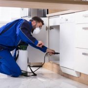 Man spraying pesticide inside the wooden cabinet in the kitchen