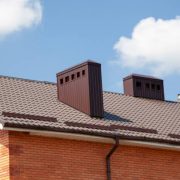Red metal roof tile and smokestack. modern chimney on brown roof.