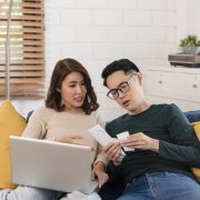 Serious-asian-husband-checking-analyzing-statement-utilities-bills-sitting-together-home