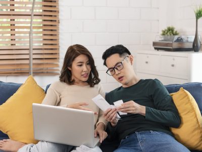 Serious-asian-husband-checking-analyzing-statement-utilities-bills-sitting-together-home