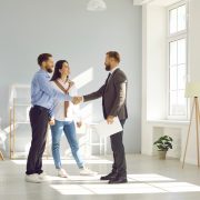 Happy young couple make deal, buy new house and shake hands with real estate agent