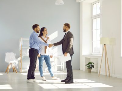 Happy young couple make deal, buy new house and shake hands with real estate agent