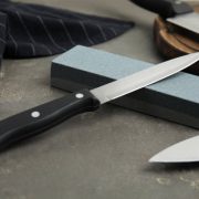 Sharpening stone and knives on grey table, closeup