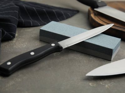 Sharpening stone and knives on grey table, closeup