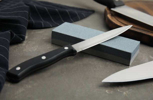 Sharpening stone and knives on grey table, closeup
