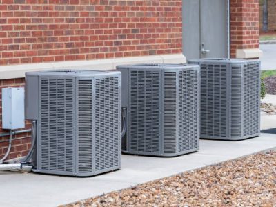 Horizontal shot of commercial air conditioners outside near a maintenance door.
