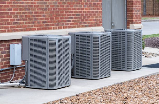 Horizontal shot of commercial air conditioners outside near a maintenance door.