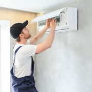 Smiling young male electrician repair conditioner in client home. man mechanic or repairman fix filters in air condition device at customer house