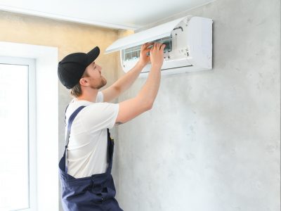 Smiling young male electrician repair conditioner in client home. man mechanic or repairman fix filters in air condition device at customer house