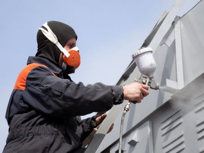 A commercial painter on the stairs spray painting a steel exteri