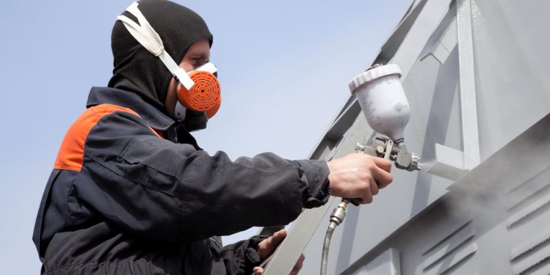 A commercial painter on the stairs spray painting a steel exteri