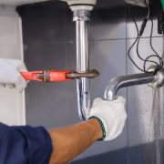 Plumber fixing white sink pipe with adjustable wrench.