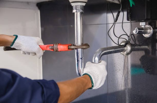 Plumber fixing white sink pipe with adjustable wrench.