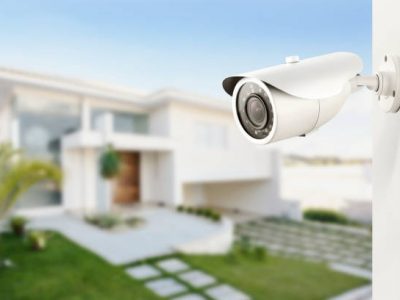 Three quarter view of varifocal surveillance camera, with a house on background