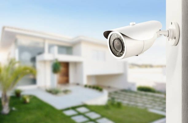 Three quarter view of varifocal surveillance camera, with a house on background