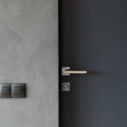 Light switch on the gray textured wall next to the door with metallic handle