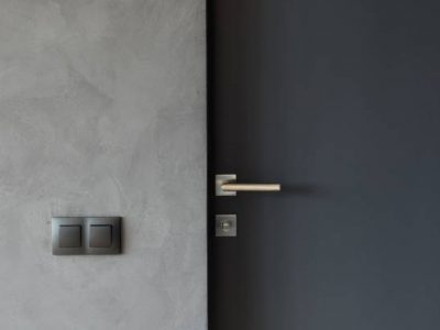 Light switch on the gray textured wall next to the door with metallic handle