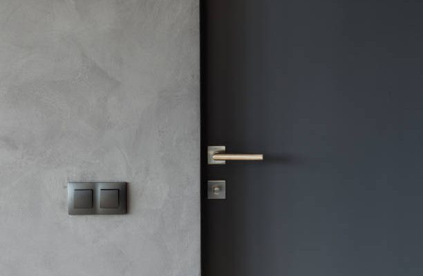 Light switch on the gray textured wall next to the door with metallic handle