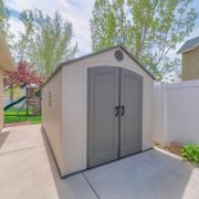 A premade shed in the backyard by the buildings and trees under the sunlight