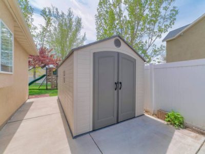 A premade shed in the backyard by the buildings and trees under the sunlight