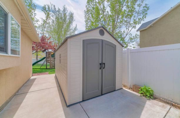A premade shed in the backyard by the buildings and trees under the sunlight