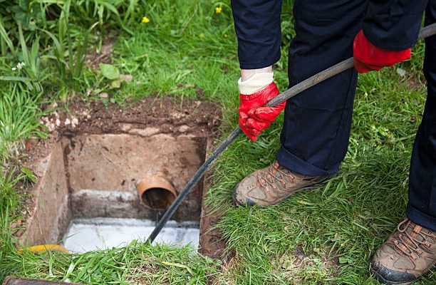 Drain being cleared by worker in navy overalls.