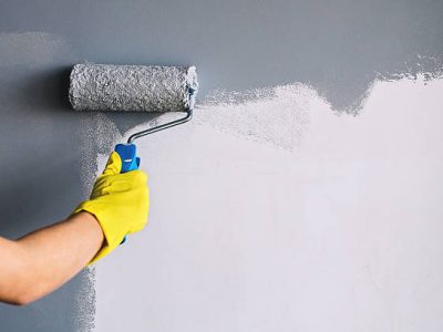 Hand in yellow glove painting wall in gray color with a roller brush.