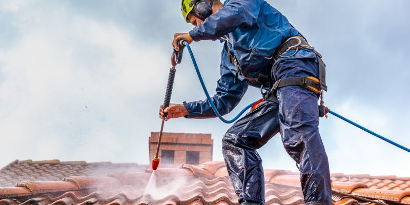 Worker washing the roof with pressurized water
