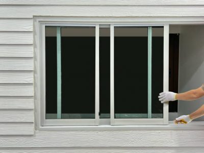 Construction worker repairing the sliding window on artificial woods siding.