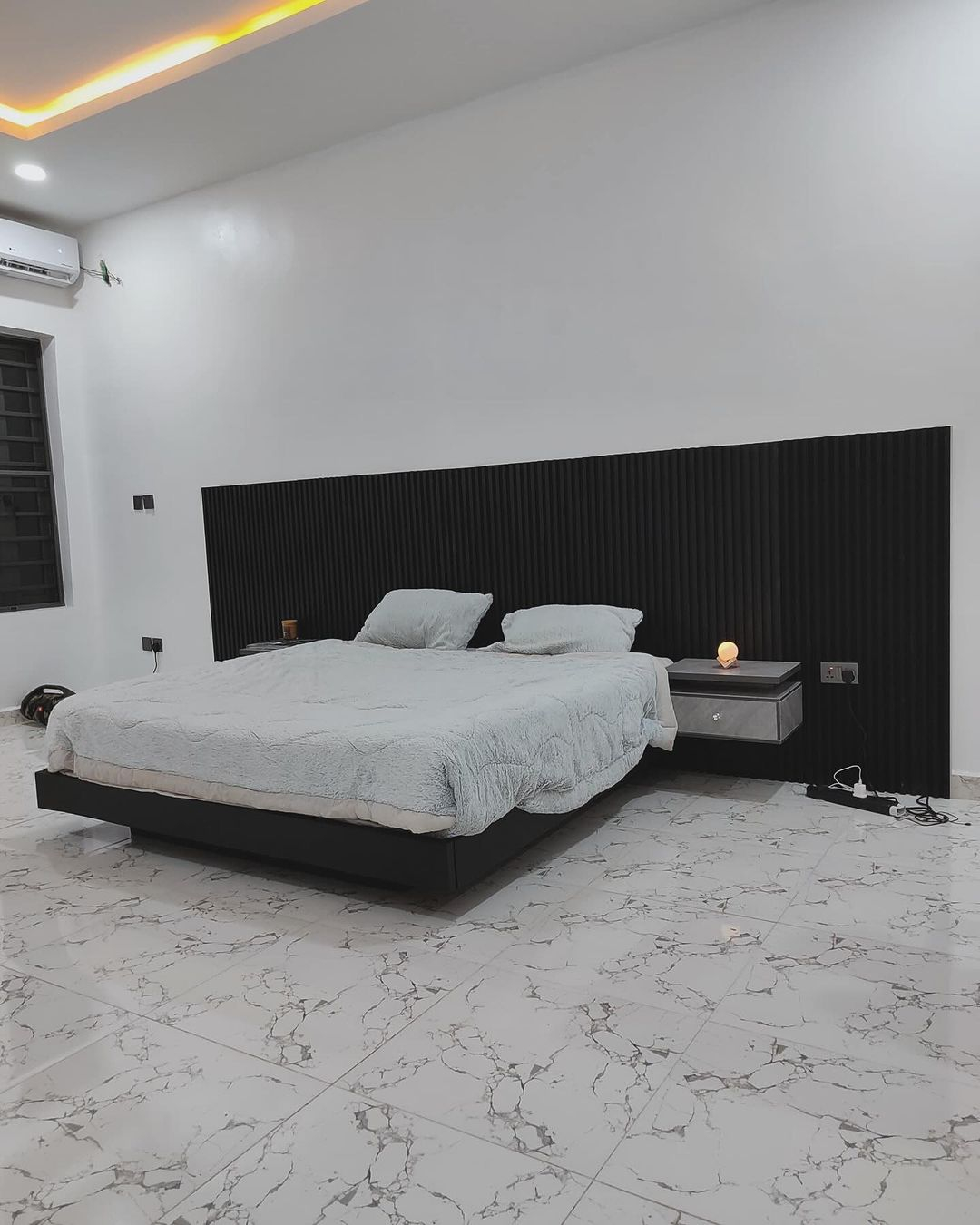 This bedroom has a black bed frame with a black headboard. You can see the floating side table there which is provided in grey color.